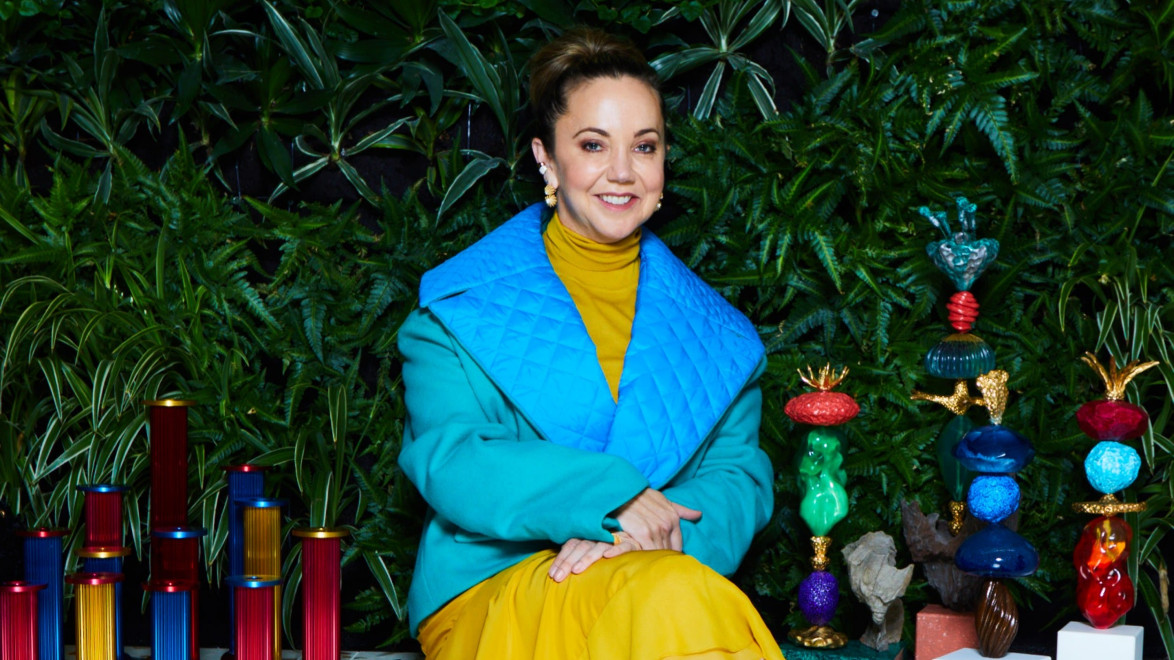 Person in colorful outfit sitting with artistic sculptures and green leafy backdrop