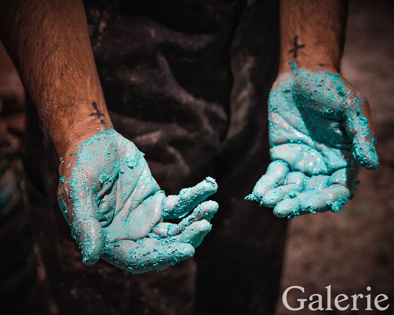 Hands covered in vibrant blue pigment, forearms tattooed, suggesting creative artistic activity or craftwork.