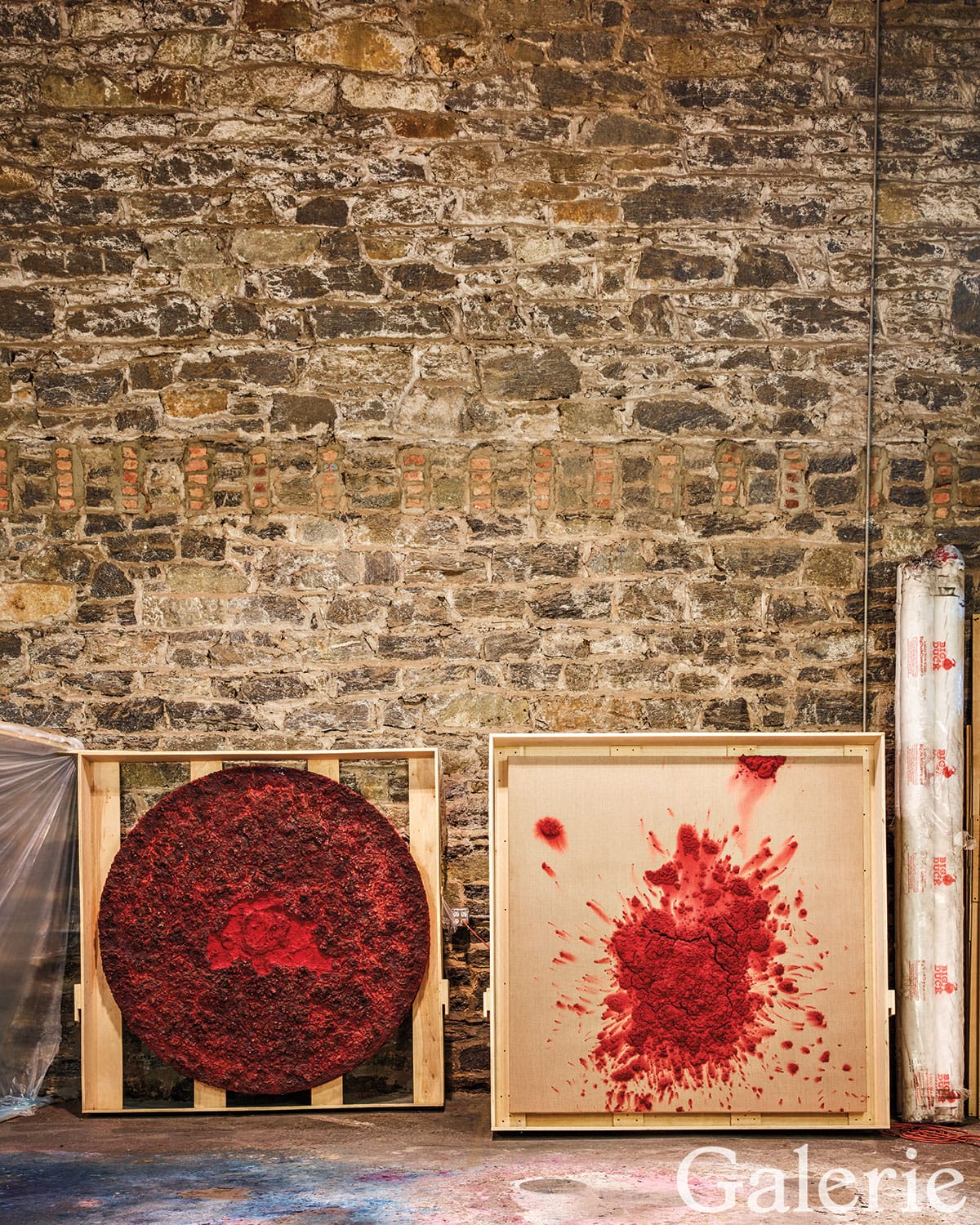 Two abstract red artworks on canvases against a rustic stone wall, featuring circular and splattered designs.