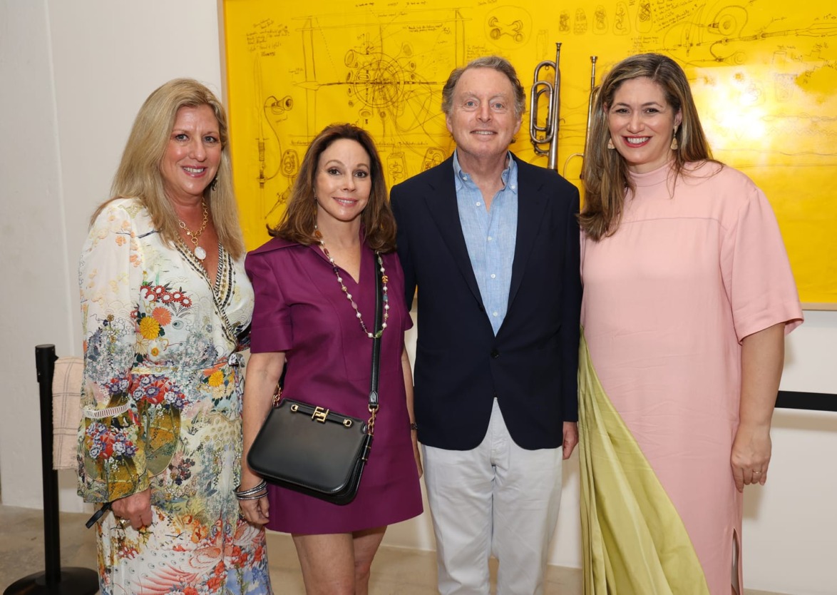 Four people smiling in front of a large yellow artwork at an indoor event.