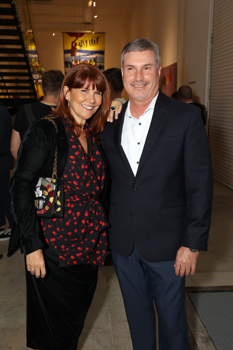 A smiling couple posing together in a gallery with artwork on the walls in the background.