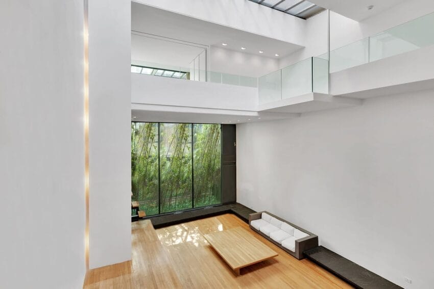 Spacious modern living room with high ceilings, large windows, white walls, and minimalistic furniture, overlooking a bamboo garden.
