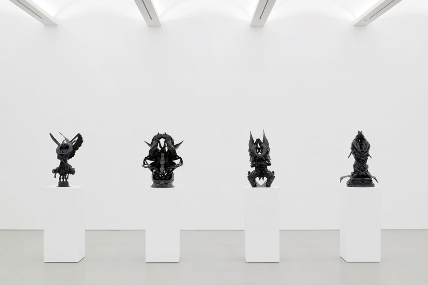 Four intricate black sculptures displayed on white pedestals in a modern gallery with a minimalist design.