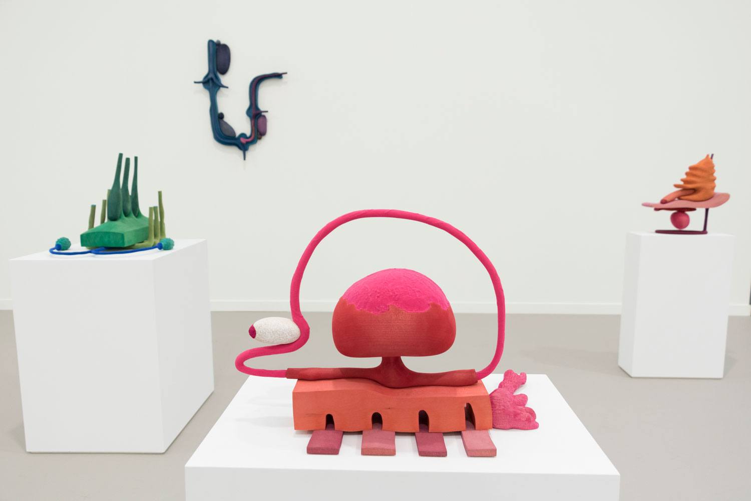 Colorful abstract sculptures displayed on white pedestals in a minimalist gallery setting.