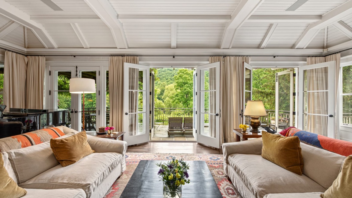 Spacious living room with sofas, lamps, and large windows opening to a scenic view of trees and greenery.