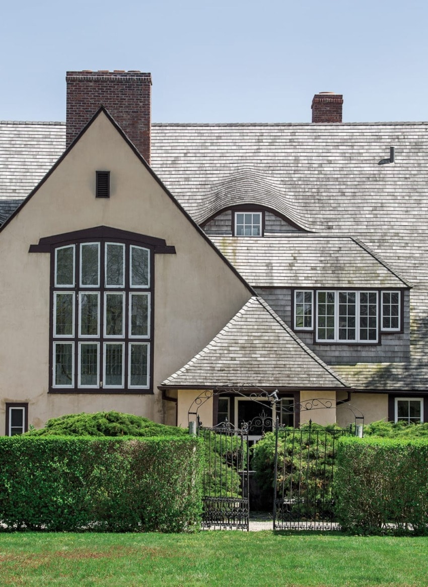 Large house with a unique roof design, large windows, landscaping, and a wrought-iron gate in front yard.
