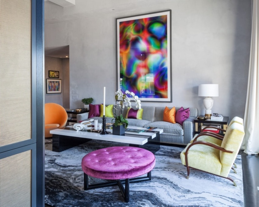 Colorful living room with vibrant abstract art, modern furniture, and diverse seating options on a patterned rug.