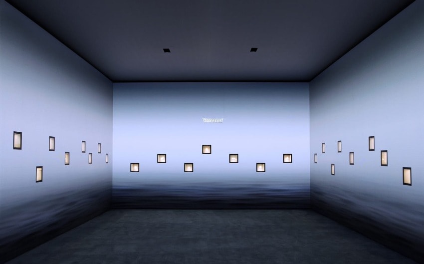 Art installation in a minimalist room with soft lighting, featuring framed images on walls, creating a serene atmosphere.