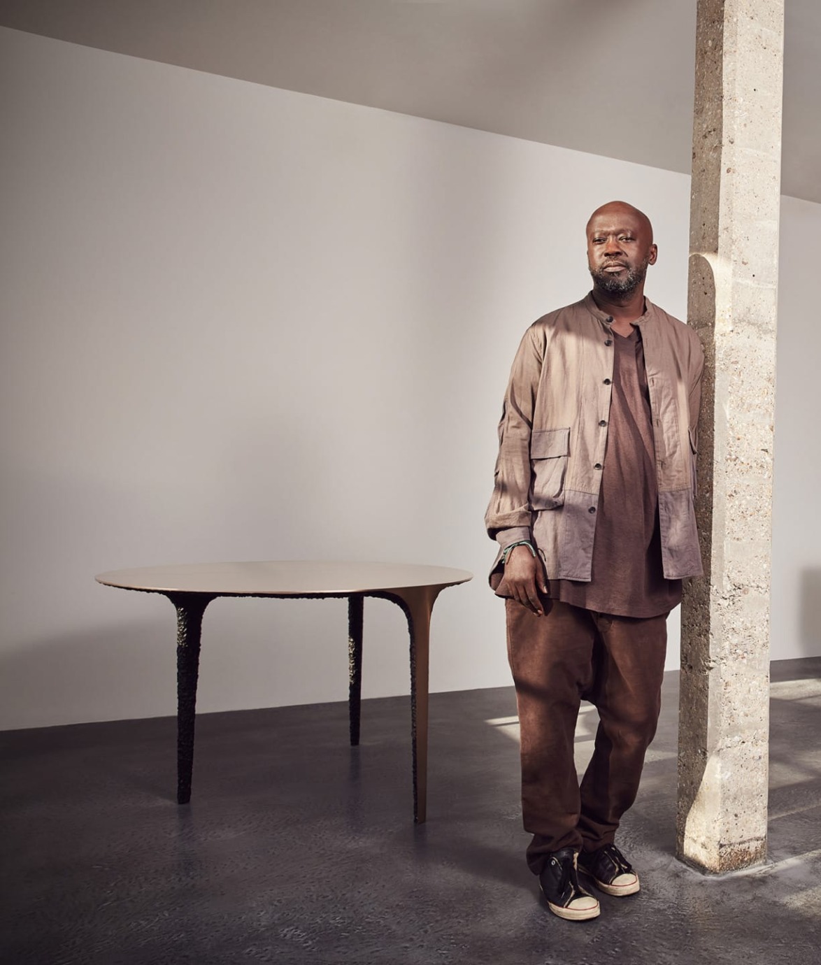 Man standing next to a modern table and stone pillar in a minimalist room.