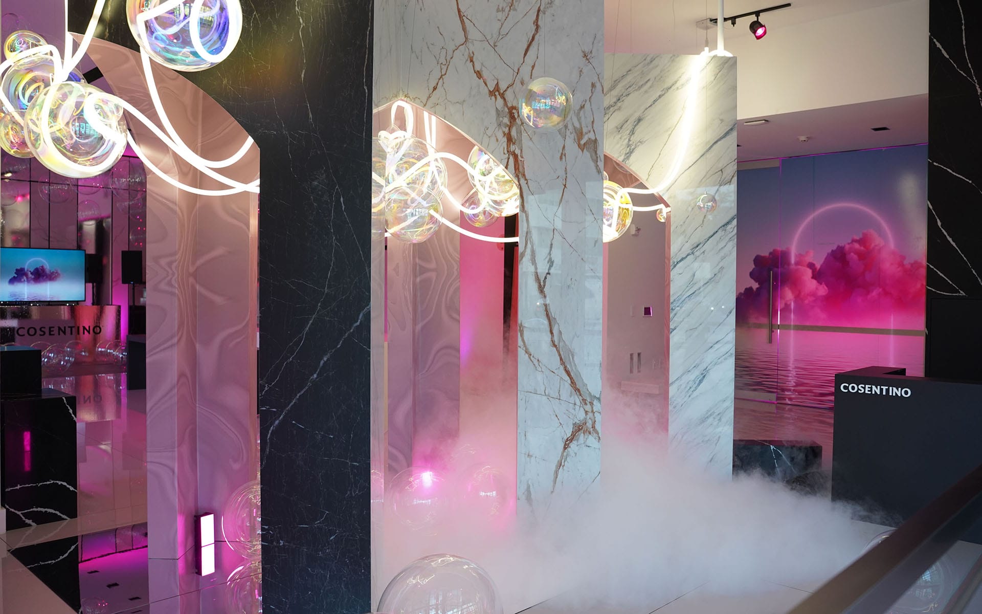 Modern art installation with colorful lights, white marble pillars, floating bubbles, and pink decorative elements.