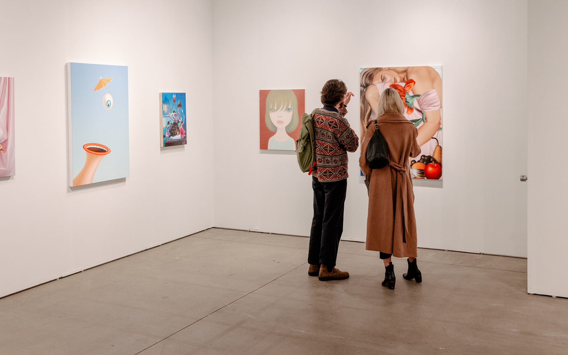 Two people observing artwork in a gallery featuring modern paintings on white walls.