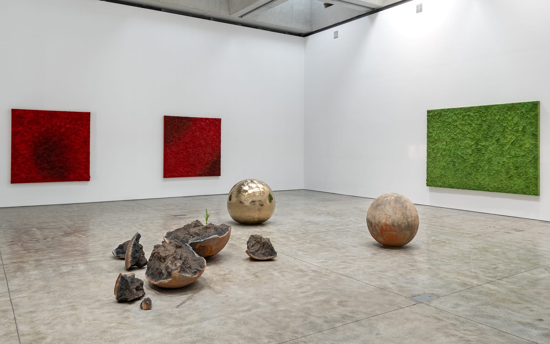 Art gallery with abstract red and green paintings; metallic and stone sculptures are placed on the gallery floor.