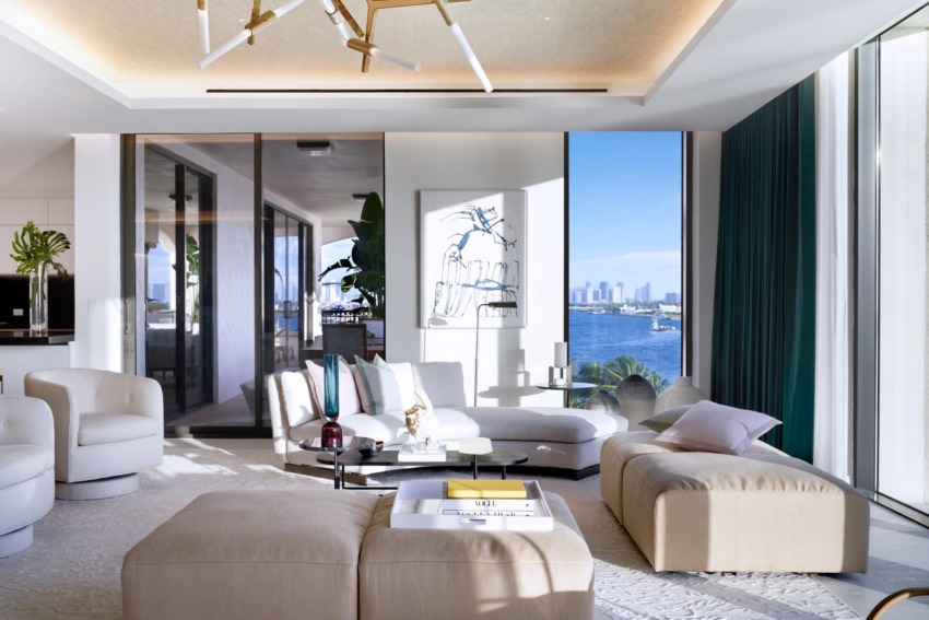 Modern living room with large windows, white sofas, decorative ceiling light, and city skyline view.