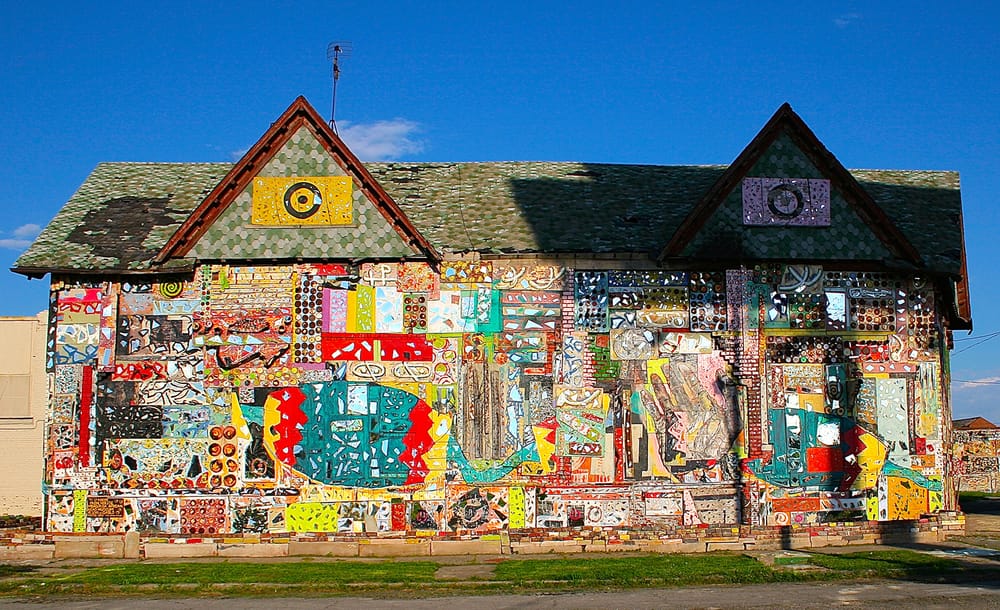 House exterior covered in vibrant mosaic artwork with various colorful patterns and designs under a clear blue sky.