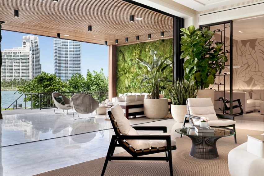 Luxurious open-air lounge with modern furniture, green wall, large plants, city skyline, and waterfront view in the background.