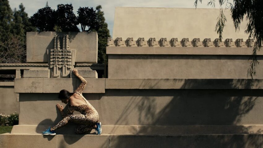 Dancer in a leopard-patterned suit poses against a modern architectural structure with intricate designs.