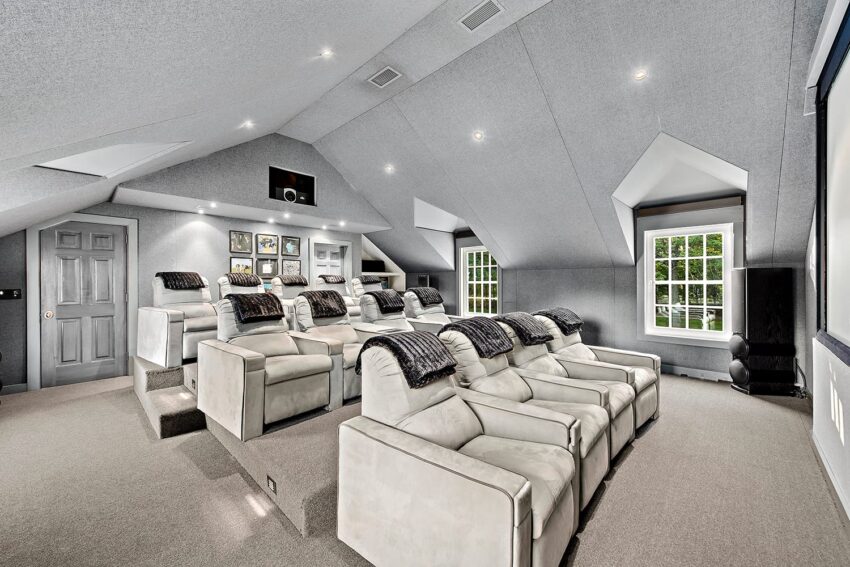 Luxury home theater with multiple rows of plush seating, large screen, and framed art on sloped gray walls.