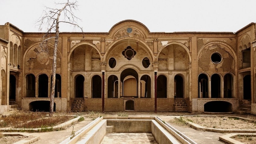 Abandoned historical building facade with arched windows and a dry tree, set against a clear sky.