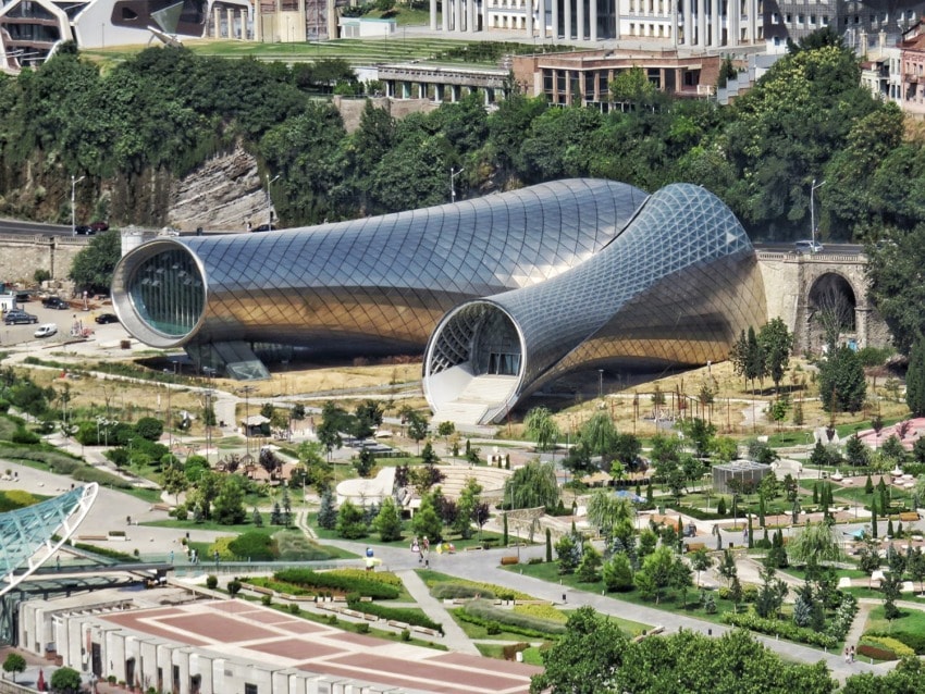 Modern architectural structure with a tubular design, surrounded by greenery and located in a vibrant urban area.