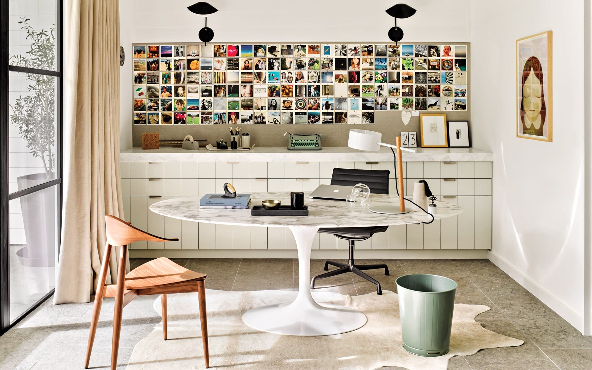 Modern home office with white cabinets, round table, wooden chair, photo wall collage, and sleek décor elements.