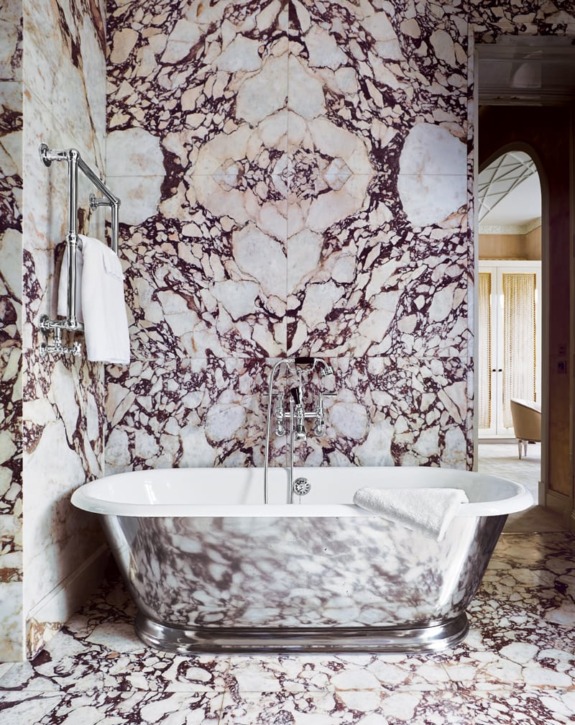 Luxury bathroom with marble walls and floor, featuring a freestanding bathtub and towel rack.