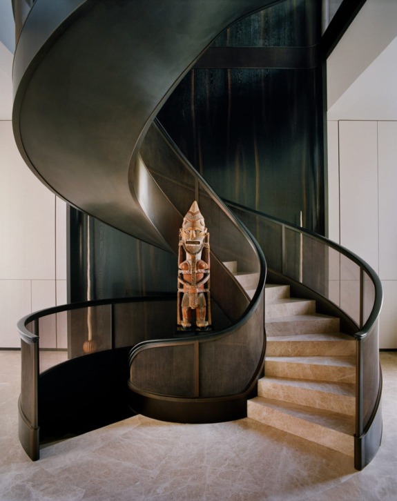 Spiral staircase with dark wood accent and an intricately carved statue at the base, set in a modern interior.