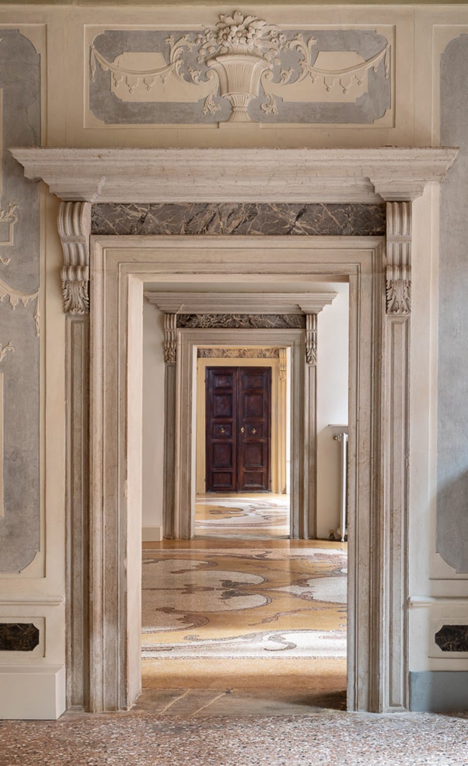 Ornate architectural view of aligned doorways in a historical building, showcasing elegant moldings and marbled floors.