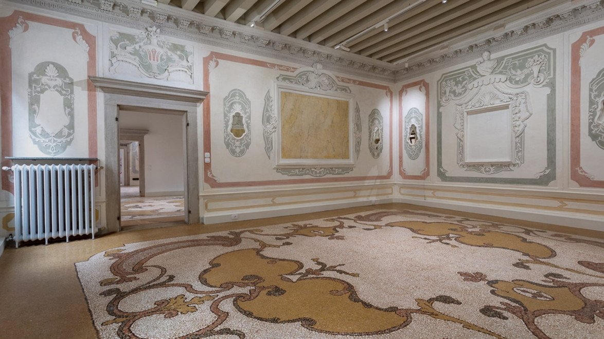 Ornate room with elaborate moldings, empty picture frames, detailed mosaics on the floor, and intricate painted designs on walls.