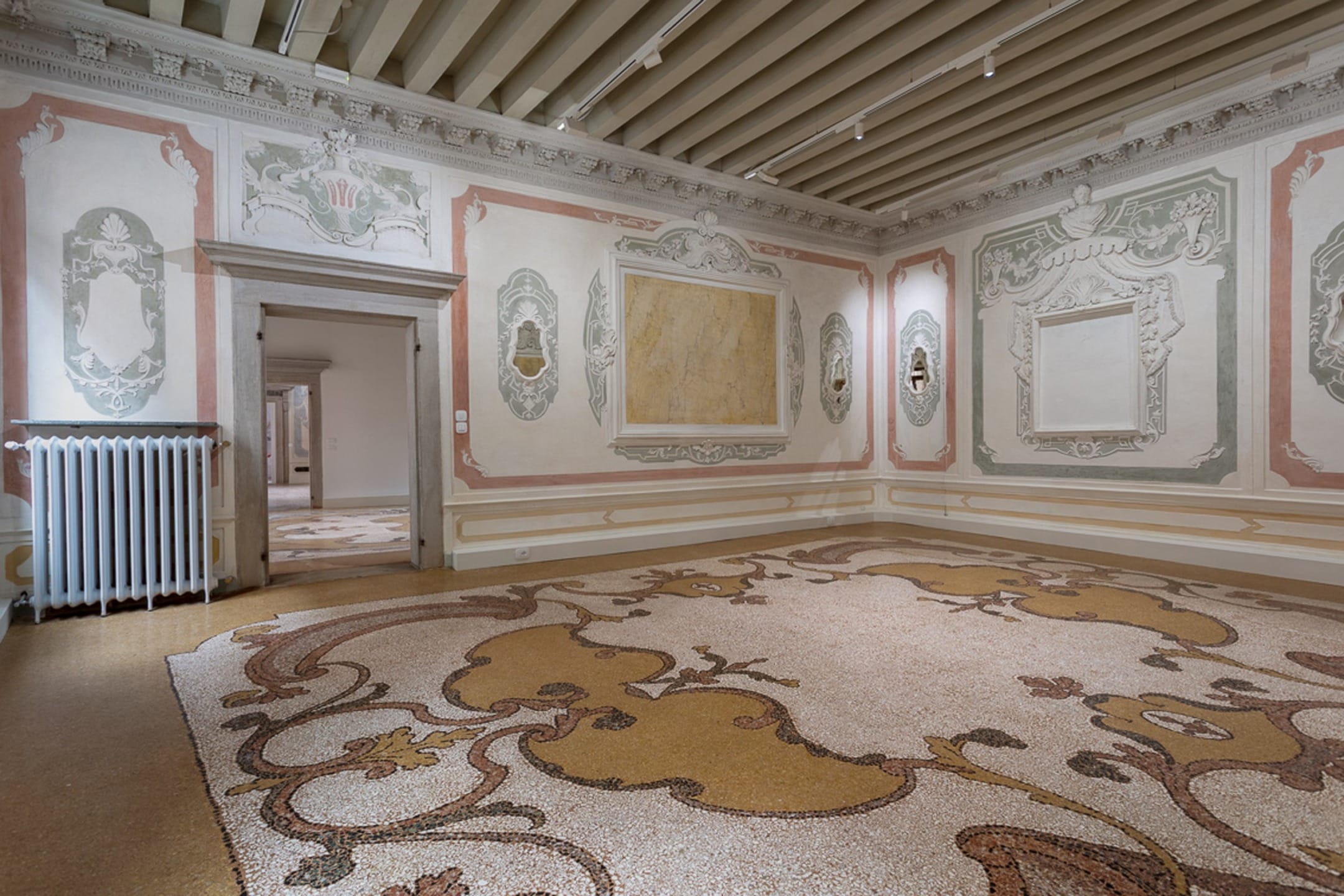 Ornate room with elaborate moldings, empty picture frames, detailed mosaics on the floor, and intricate painted designs on walls.