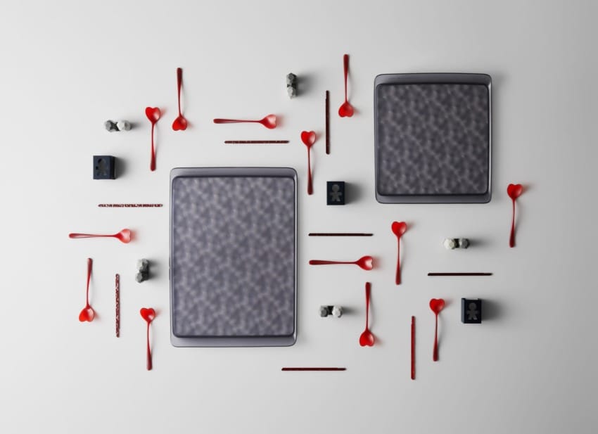 Two large rectangular cookies surrounded by red heart-shaped spoons and small decorative black and white food items on white background