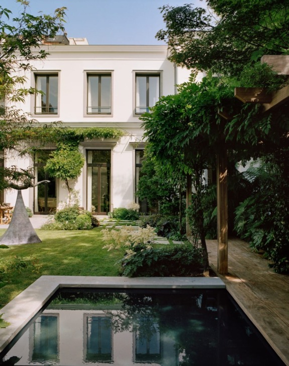 Elegant two-story white house with lush garden and reflecting pool under clear blue sky.
