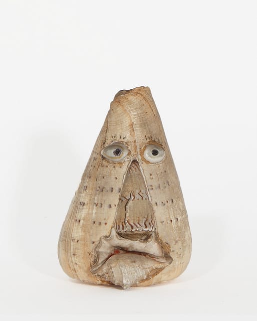 Carved wooden face with exaggerated features, including large eyes and mouth, on a plain white background.