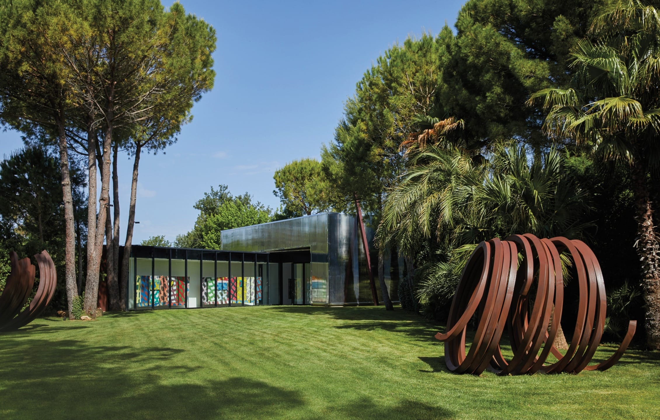 Modern art museum surrounded by trees and greenery, with a sculpture of circular metal rings on the lawn.