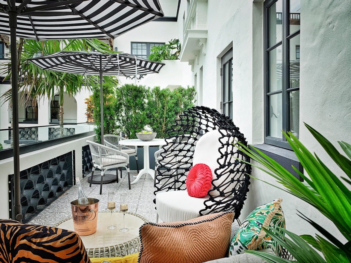 Stylish outdoor patio with modern furniture, a cozy round chair, striped umbrellas, and lush greenery.
