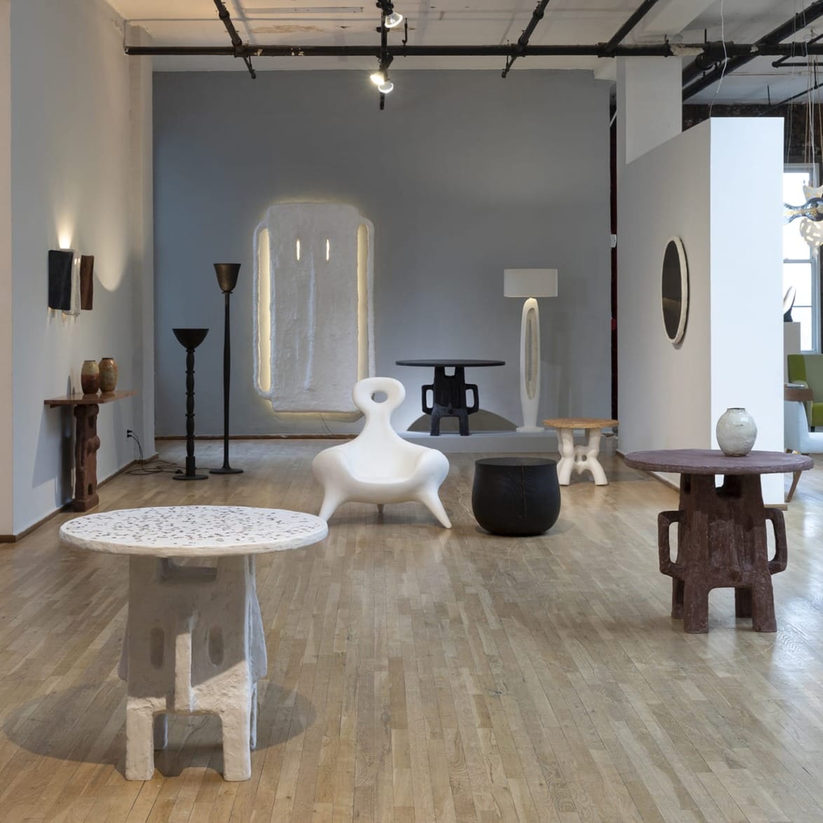 Exhibit room with various contemporary furniture pieces arranged on a wooden floor, including tables and a unique white chair.