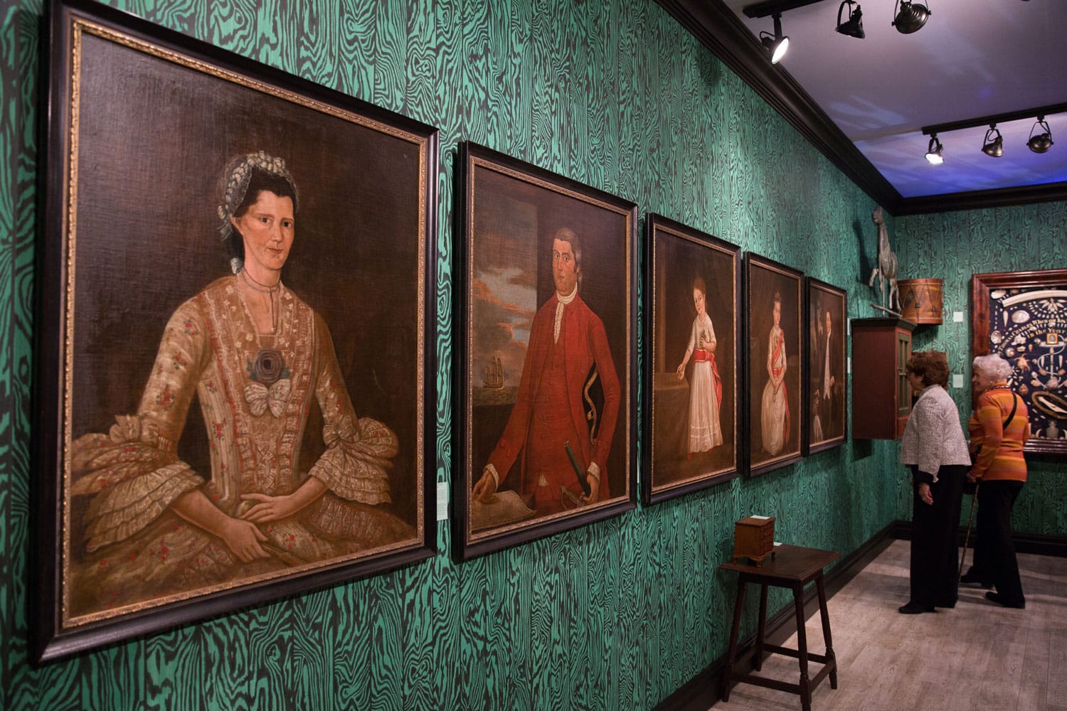 Visitors viewing historical portraits in a museum gallery with green patterned walls.