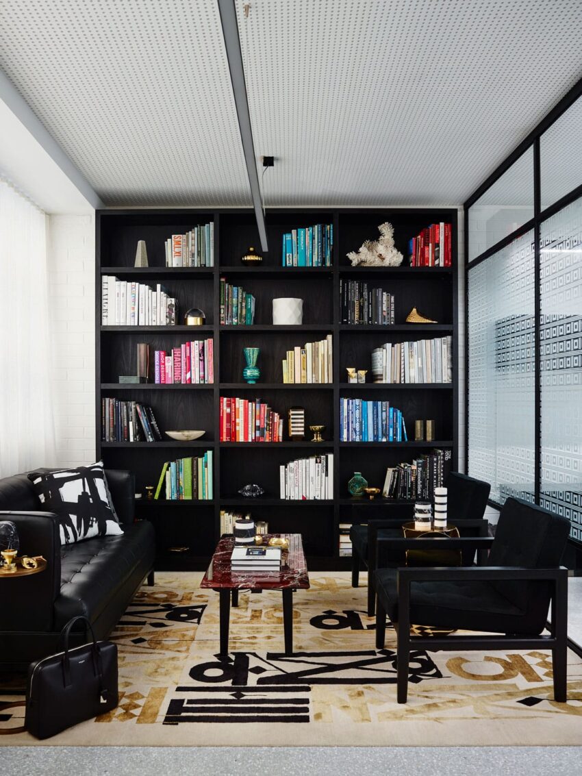 Modern office with black shelves, colorful books, stylish black furniture, abstract rug, and decorative items.