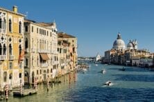 Venice Grand Canal with historic buildings, boats on water, and blue sky in the background.