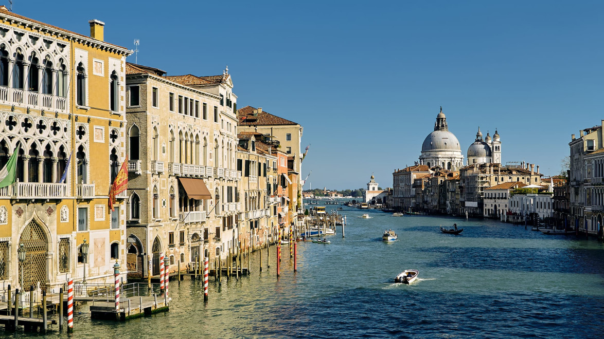 Venice Grand Canal with historic buildings, boats on water, and blue sky in the background.
