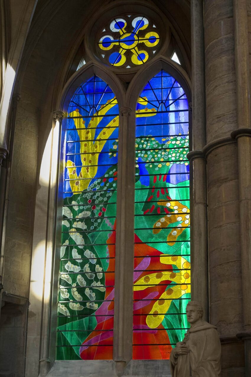 Colorful stained glass window in a cathedral with abstract patterns and a stone statue in the foreground.
