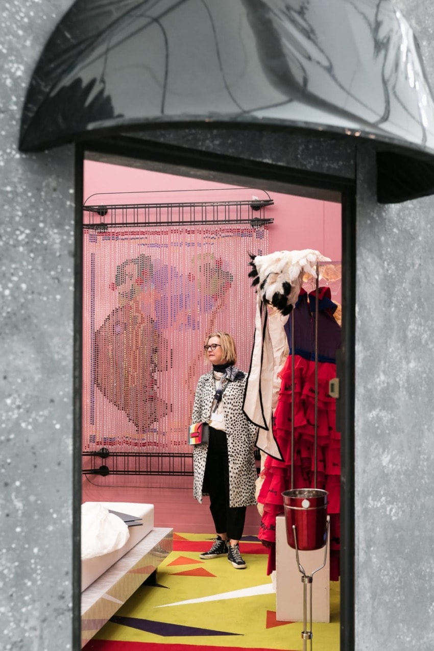 Woman in stylish outfit stands in a colorful, modern room with artistic decor and vibrant patterns.