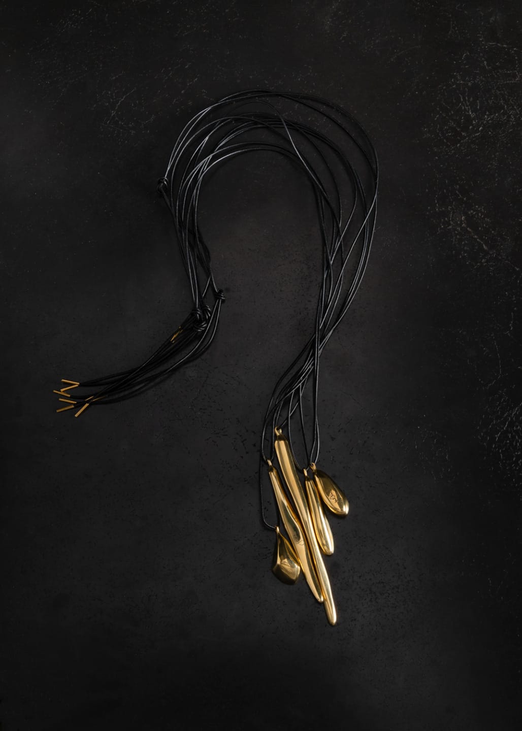 Black cords with gold pendants on a dark surface.
