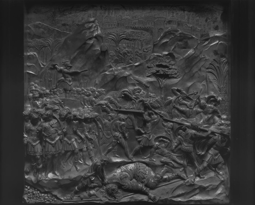 Historical relief depicts a detailed battle scene with soldiers, armor, weapons, and a fallen warrior amidst a rugged landscape.