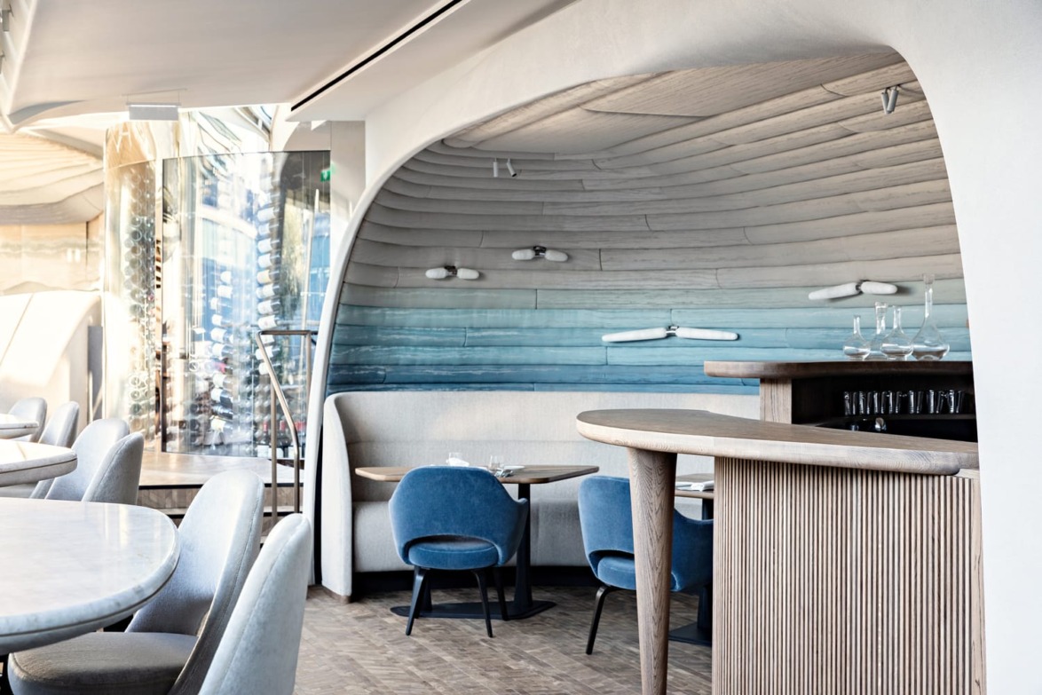 Modern restaurant interior with arching wooden ceiling, stylish blue and grey furniture, and minimalist decor.