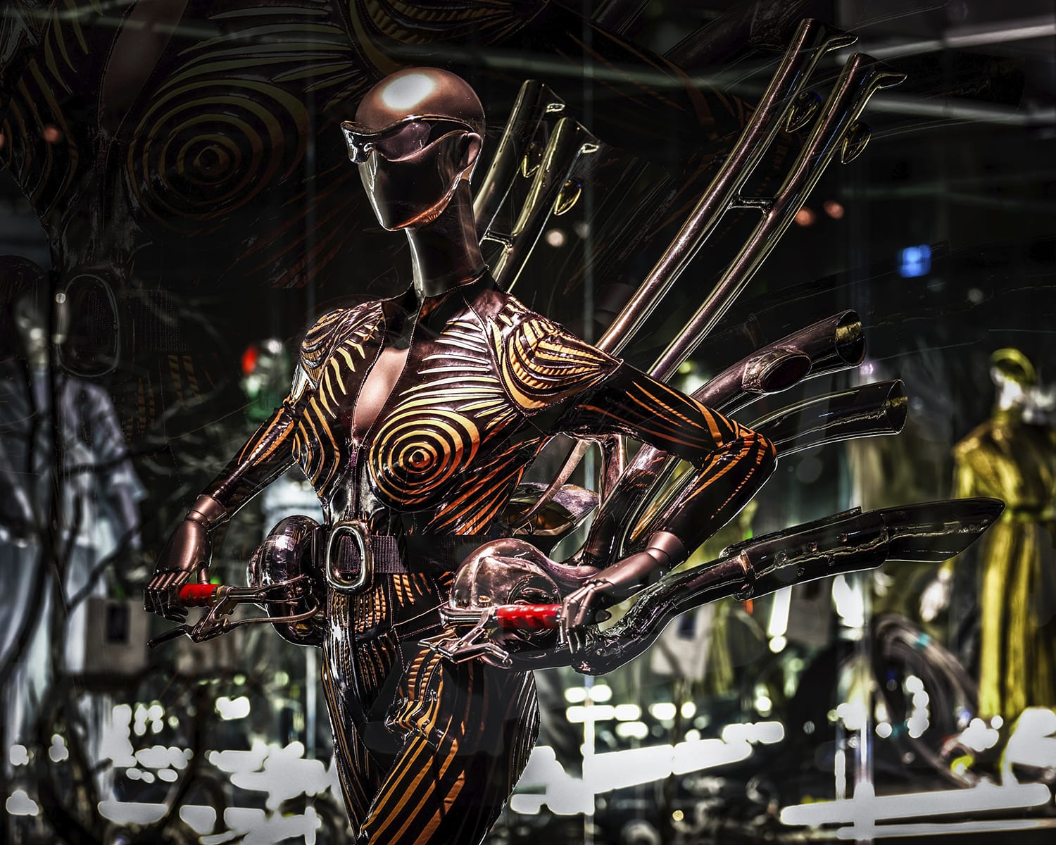 Futuristic mannequin in chrome and gold attire with intricate wing-like accessories, displayed in a stylish showroom setting.