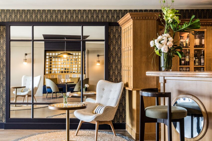 Cozy hotel lounge with a plush armchair, stylish wallpaper, elegant lighting, and a wooden bar adorned with fresh flowers.
