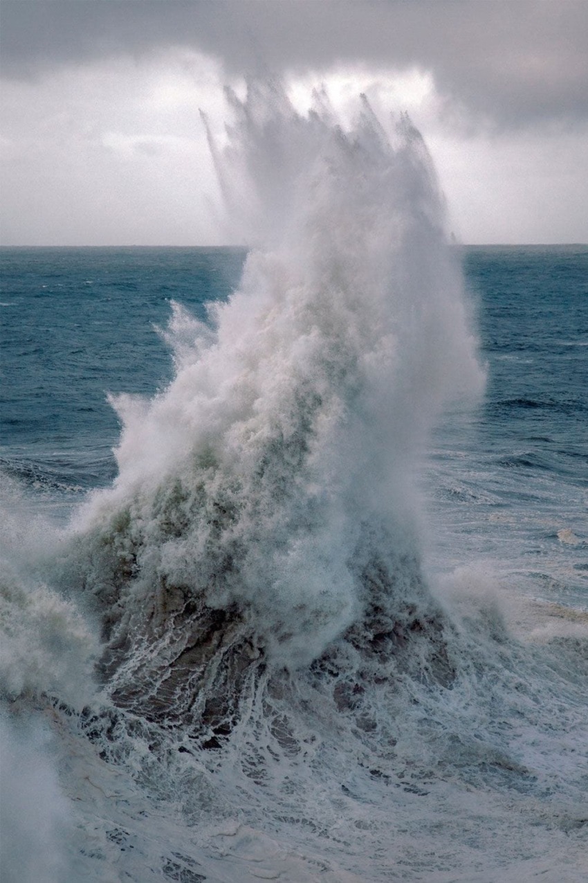 Powerful ocean wave crashing dramatically against dark, cloudy sky.