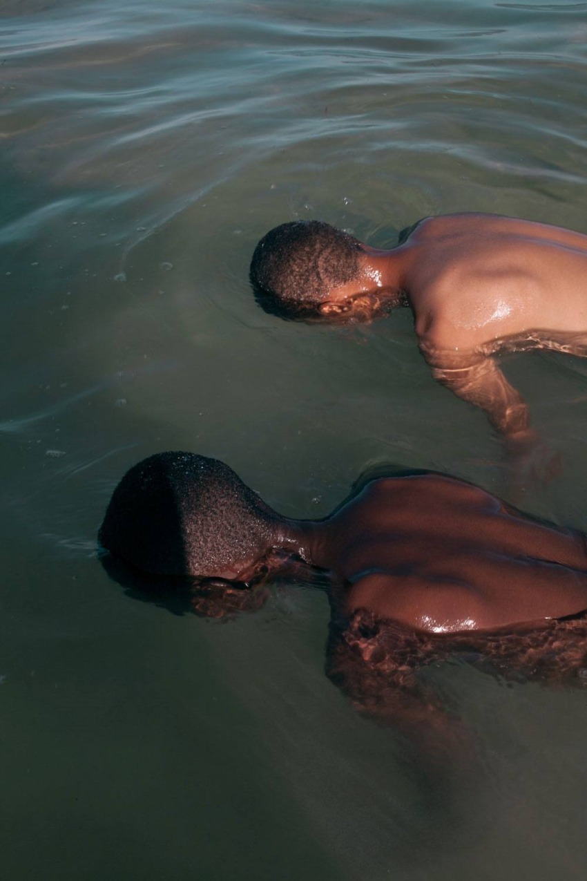 Two people submerged in water, facing downward, in a calm greenish sea.