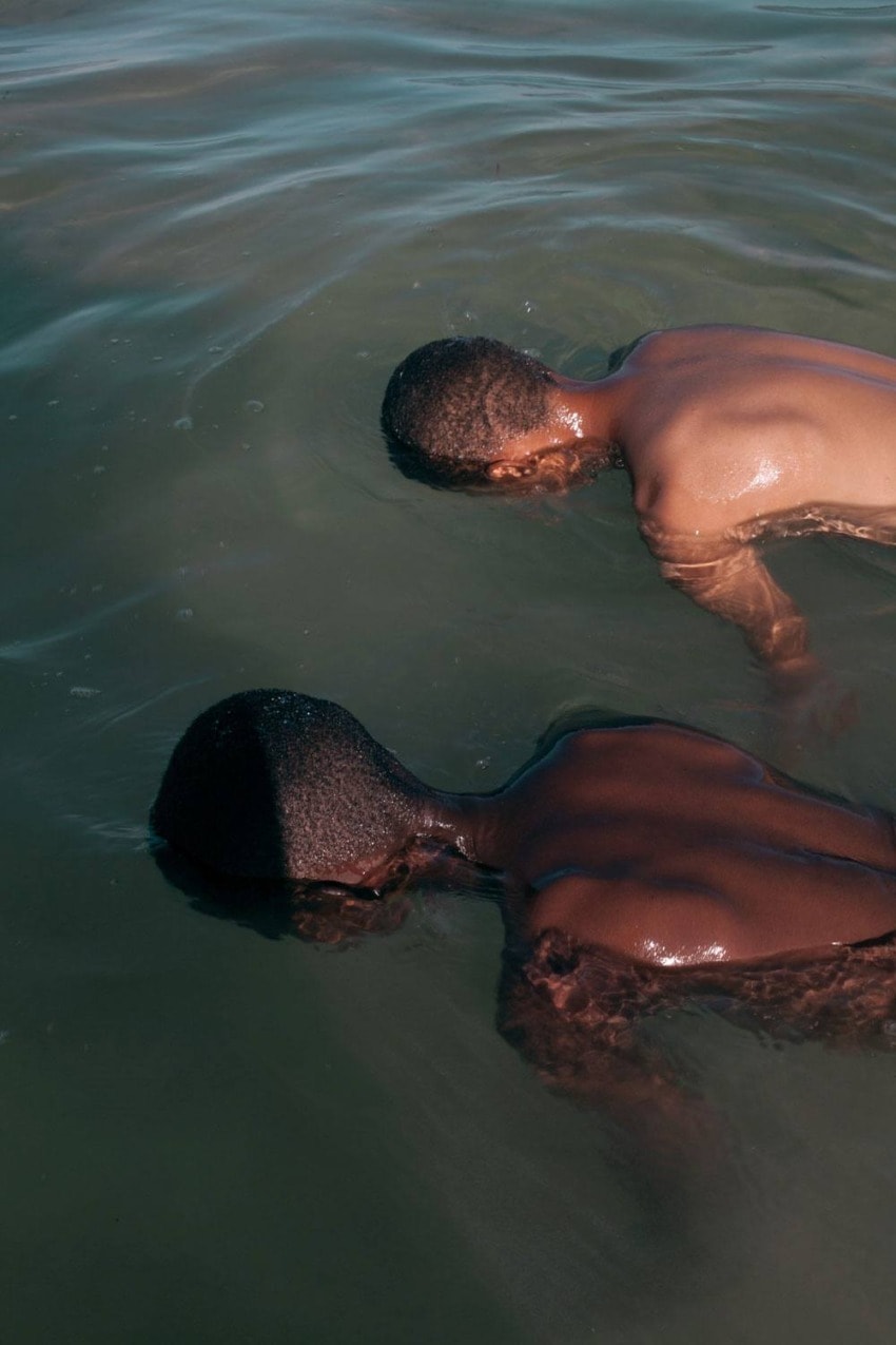 Two people submerged in water, facing downward, in a calm greenish sea.