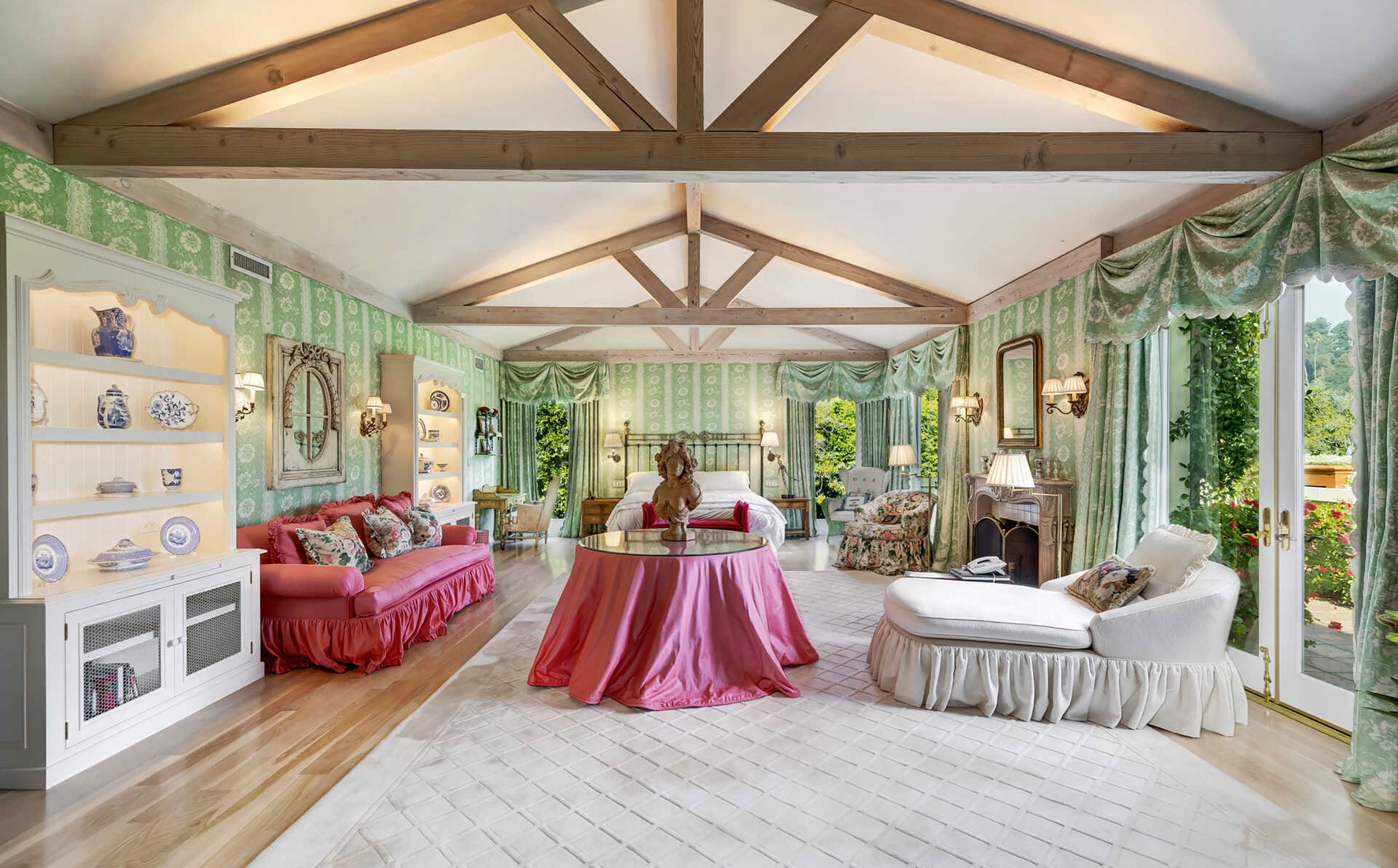 Elegant living room with exposed beams, floral wallpaper, pink and white furniture, and large windows with garden views.